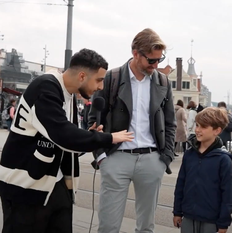 Man interviewt vader en twee kinderen op straat voor Straatvragen bij Amsterdam Centraal Station.