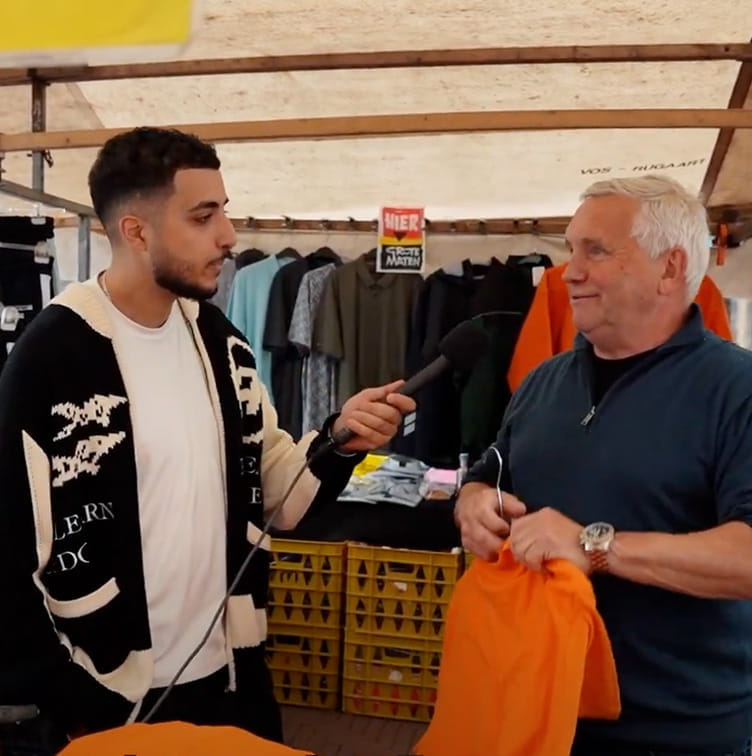 Man interviewt oudere man op de Dappermarkt met vragen over het energienet voor Straatvragen. 