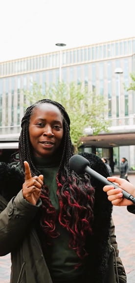 Straatinterview met een vrouw in een stedelijke omgeving, waarbij ze in gesprek is met een interviewer voor een modern gebouw.