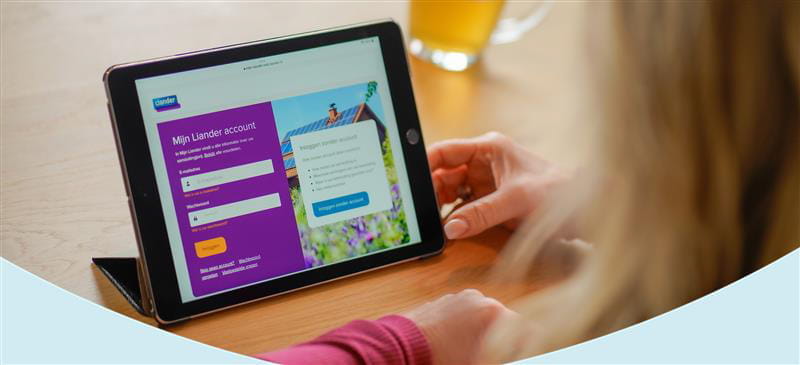 Een persoon bekijkt een tablet met daarop het inlogscherm van een "Mijn Liander" account. Op het scherm staan velden om een gebruikersnaam en wachtwoord in te voeren, en er is een afbeelding van een huis met zonnepanelen zichtbaar. Op de achtergrond staat een glas met een drankje op tafel.