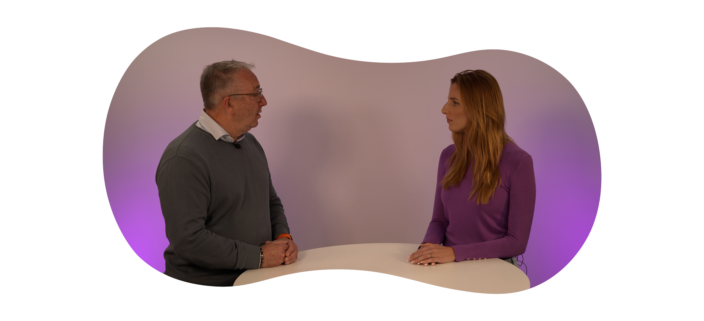 Twee personen zitten tegenover elkaar aan een ronde tafel en voeren een echt gesprek over weerbaarheid bij een langdurige stroomstoringin een studio met paarse achtergrondverlichting.