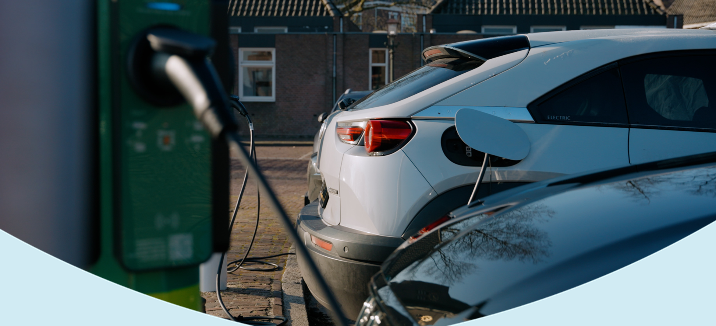 Elektrische auto aangesloten op een groene laadpaal in een woonwijk.