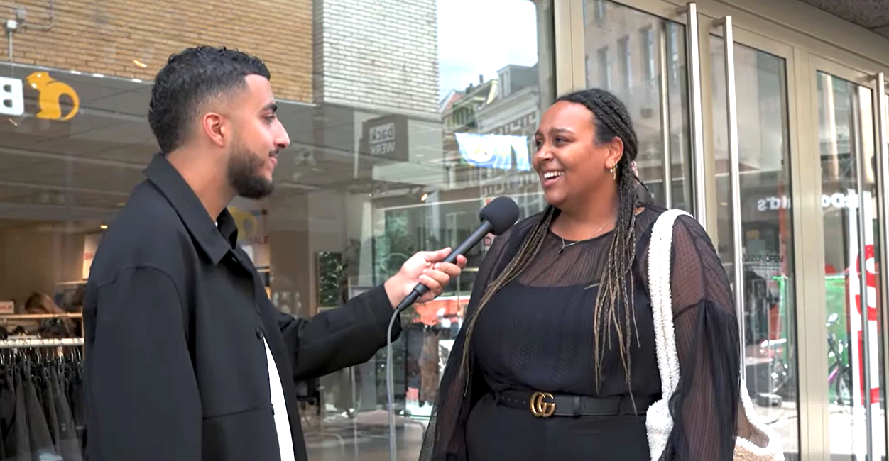 Interviewer die op straat een vrouw interviewt voor een winkelpui, waarbij de microfoon naar haar wordt uitgestoken terwijl ze met elkaar in gesprek zijn.
