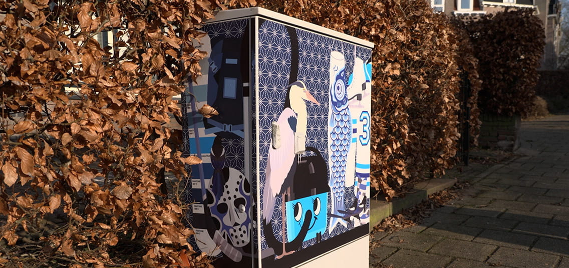 Beschilderde elektriciteitskast in een woonwijk, versierd met illustraties van een ooievaar, een uil, een hockeymasker en een lachende stekker, geplaatst naast een haag langs de stoep.