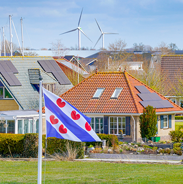 Vlag van friesland wappert in de wind. Op de achtergrond woningen met zonnepanelen en in de verte staan twee windmolens