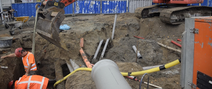 Graafmachine en medewerker aan het werk in een open sleuf in een Amsterdamse straat.