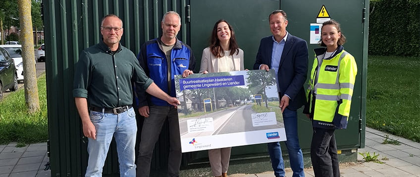 Groep personen staat voor een elektriciteitshuisje om de start van een samenwerking te vieren. Ze kijken vrolijk in de camera en houden een posterbord vast waar de details van de samenwerking op staan