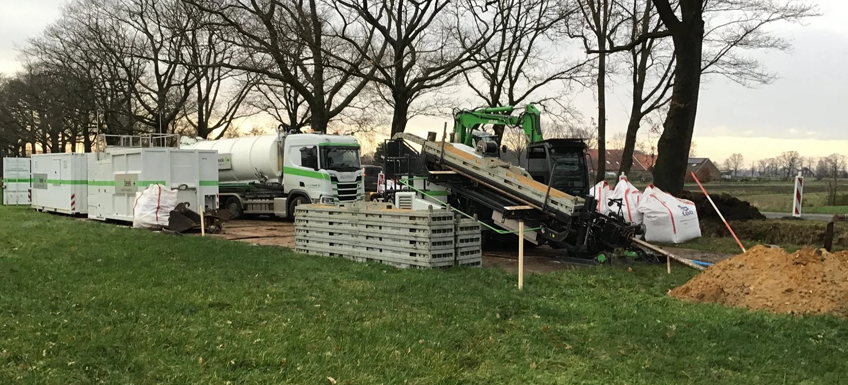 Gestuurde boring in Groenlo. Op de bouwplaats staat materialen opgestapeld en staan grote machines en vrachtwagens voor de gestuurde boring.