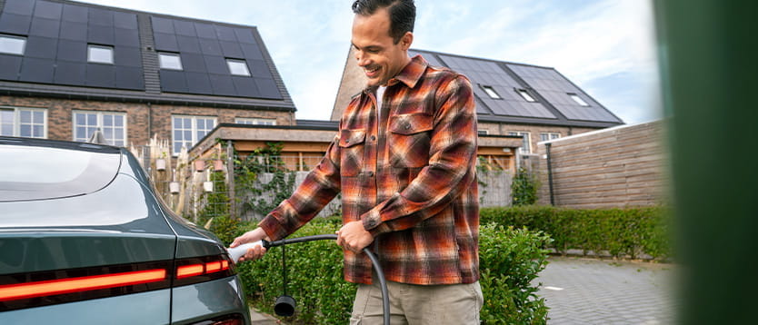 Persoon laadt een elektrische auto op voor een woning met zonnepanelen op het dak.