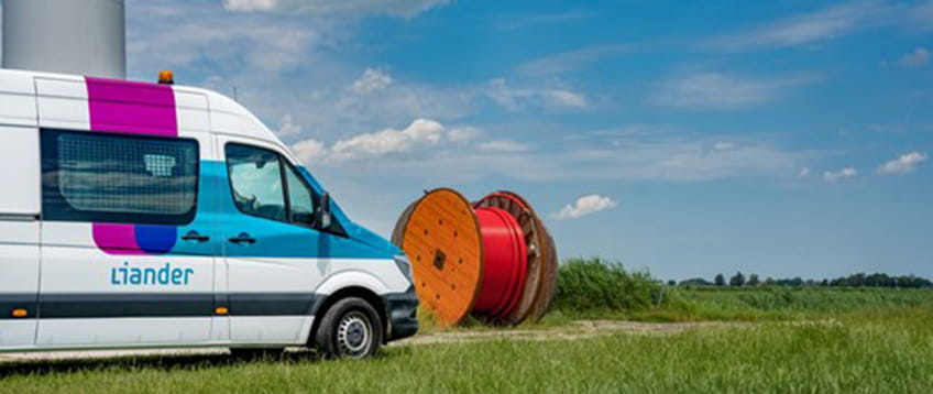 Liander werkbus staat in een weiland naar een grote haspel met rode elektriciteitskabels