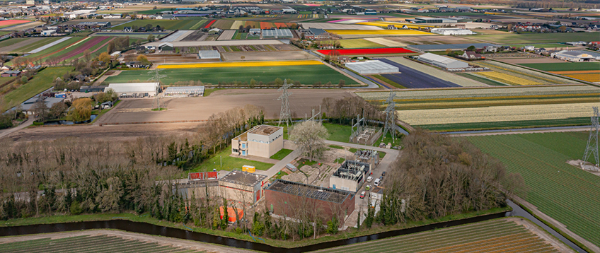 Dronefoto van het onderstation in Sassenheim, omringd door bomen en uitgestrekte weilanden in een landelijke omgeving.