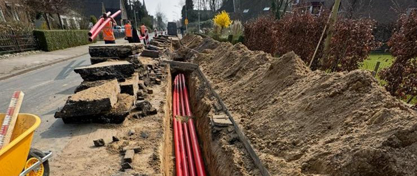 grondwerkzaamheden in de straat met een aantal dikke rode kabels in de grond. Op de achtergrond lopen werkmannen in veiligehidskleding.