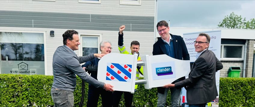 Vijf personen overhandigen symbolisch een grote sleutel met Liander-logo tijdens een openingsmoment buiten.