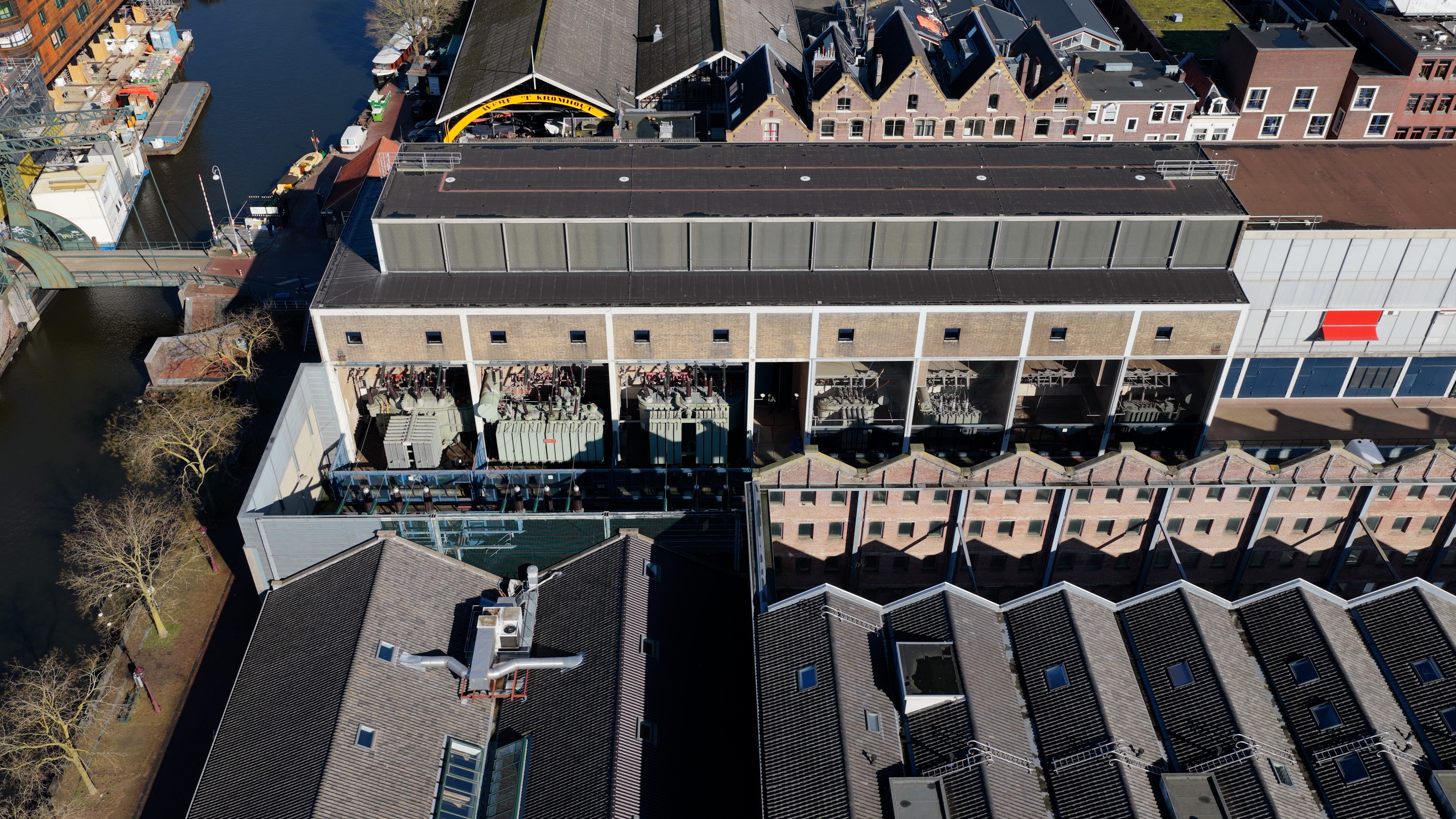 Luchtfoto van het historische elektriciteitsstation aan de Hoogte Kadijk in Amsterdam, met zicht op de bestaande gebouwen en installaties die vernieuwd worden door Liander en TenneT.