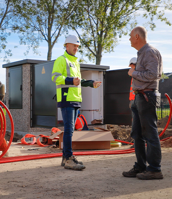 Je ziet een Liander monteur op straat in gesprek met een man.