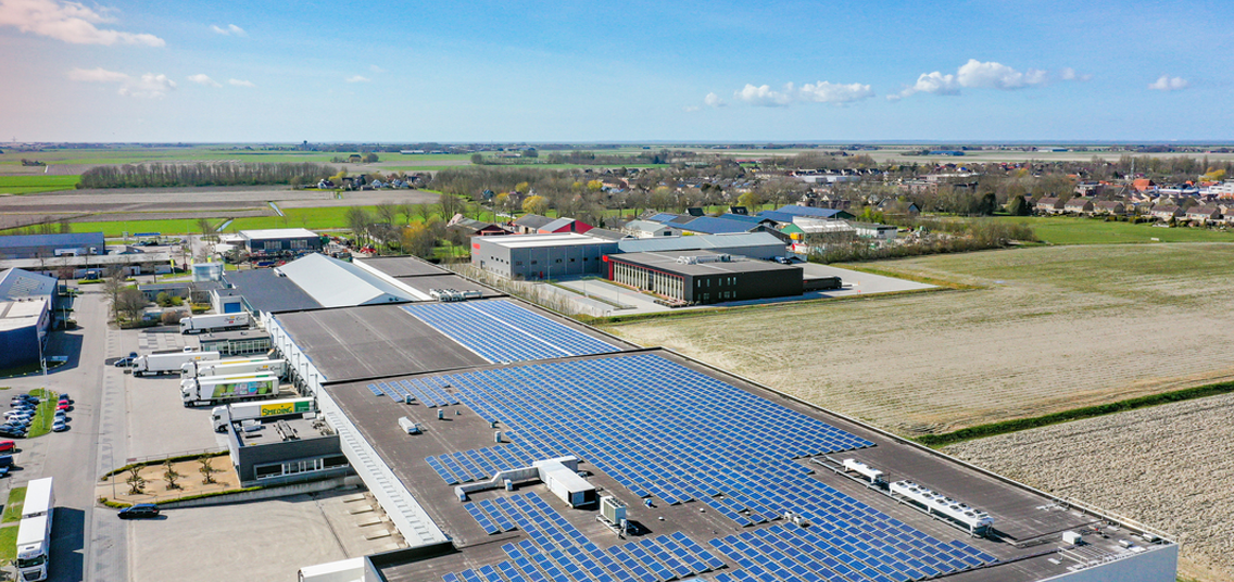 Foto vanuit de lucht genomen van een groot bedrijf met een heleboel zonnepanelen op het dak. 
