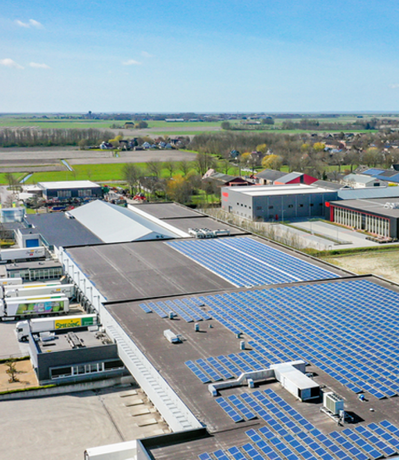 Foto vanuit de lucht genomen van een groot bedrijf met een heleboel zonnepanelen op het dak.