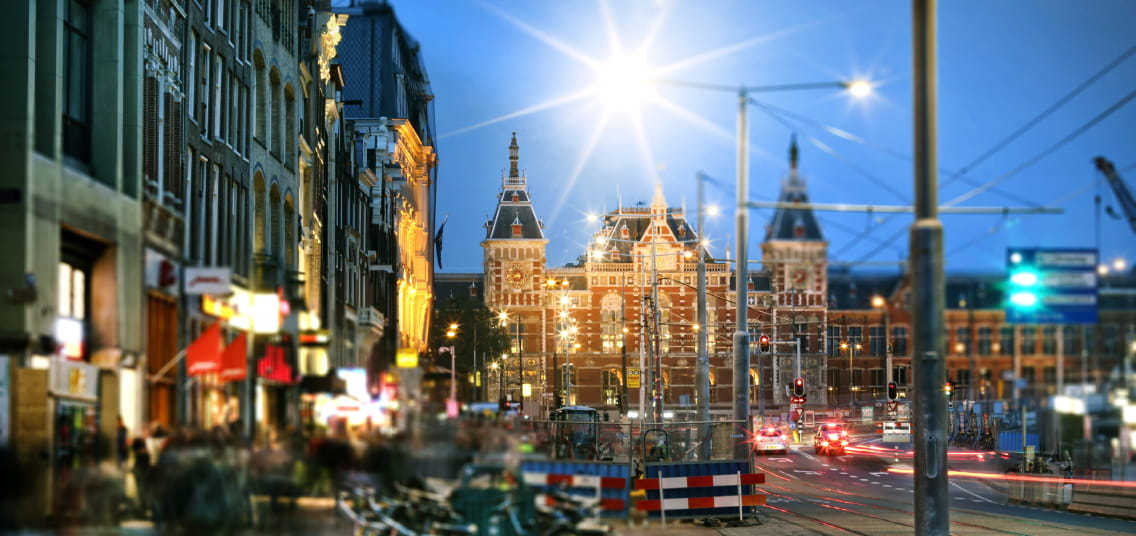 Amsterdam centraal station bij schemerlicht. De straatlantaarns zijn aan.