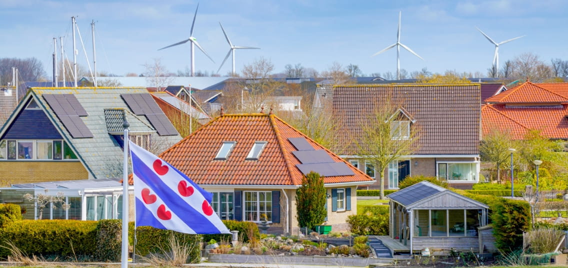Luchtfoto van woonwijk in Friesland met Friese vlag op de voorgrond en windmolens in de verte