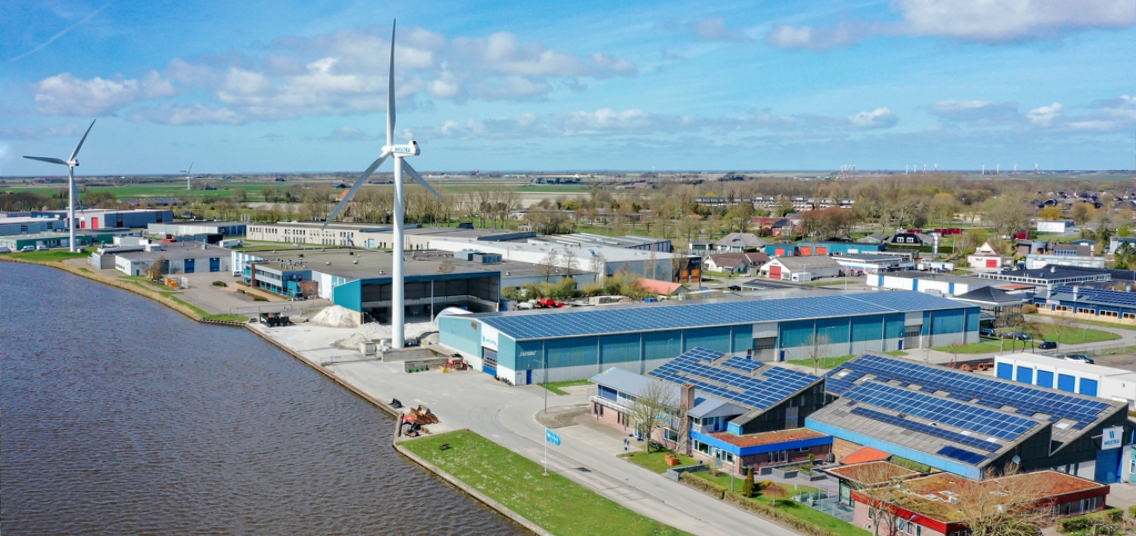 Luchtfoto van industrieterrein aan het water met windmolen en zonnepanelen op het dak