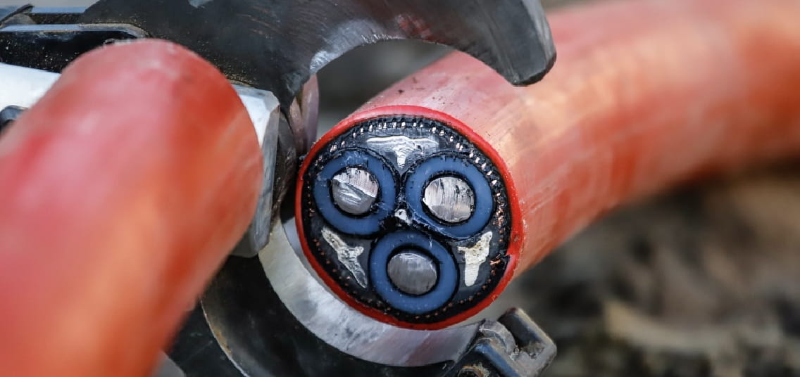 Een rode elektriciteitskabel wordt met een tang doorgeknipt. In de binnenkant die je verschillende kabels bij elkaar