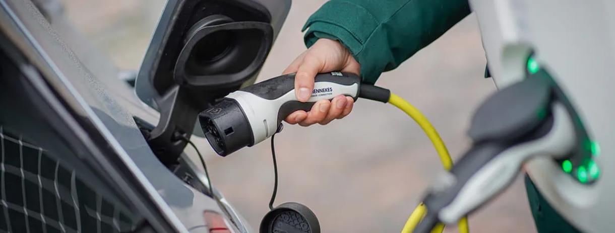 Hand die een laadstekker in de laadpoort van een elektrische auto steekt.