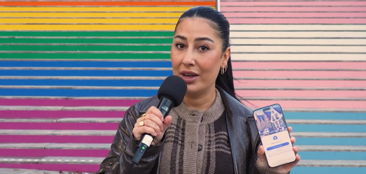 Vrouw met microfoon houdt een smartphone met app-scherm omhoog voor een kleurrijke achtergrond.