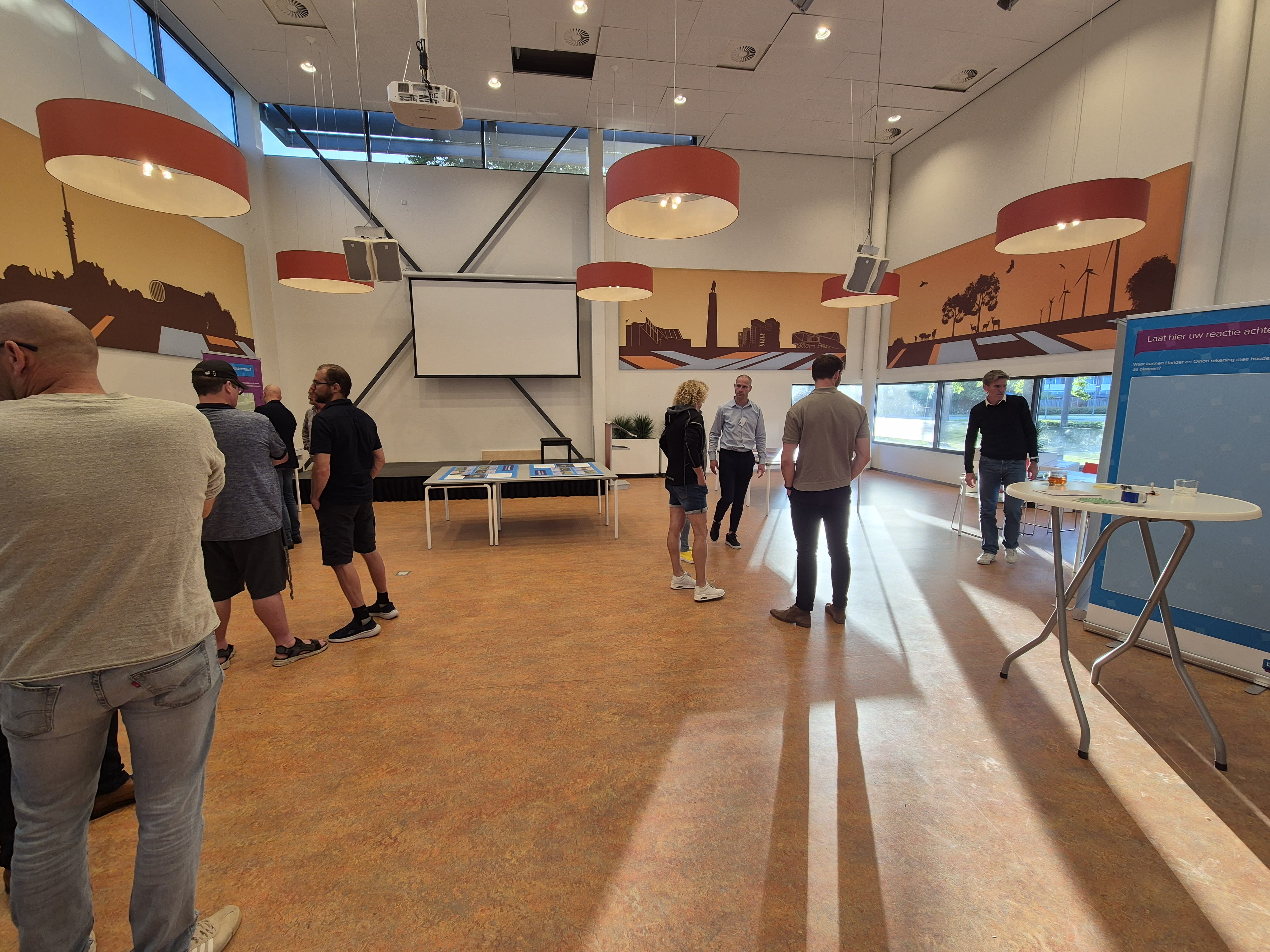 Indruk van de inloopbijeenkomst waarop bezoekers en medewerkers van Liander en gemeente Lelystad staan. Er staan posters met ontwerpen die mensen kunnen bekijken